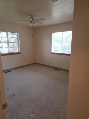 Wall-to-wall carpeting, two windows with blinds, and a ceiling fan with integrated lighting