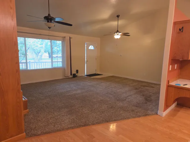 Vaulted ceilings with dual ceiling fans, large front-facing window, and wood-finish flooring