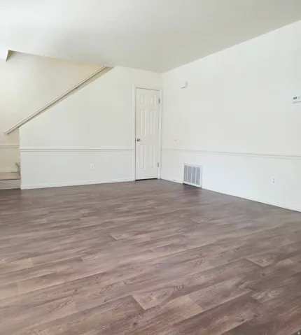 Wood-finish flooring throughout, bright white walls, white trim, and a paneled interior door