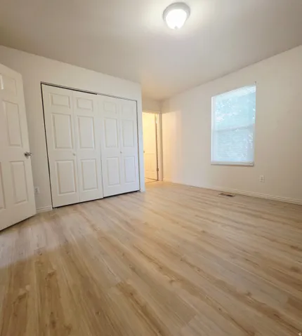 Wood-finish flooring, white walls, white trim, window with blinds, and white bi-fold closet doors