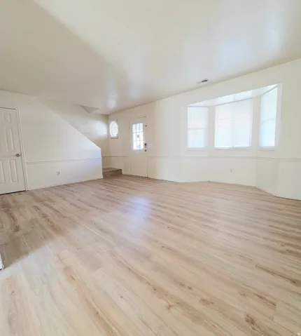 Expansive room featuring wood-finish flooring, a bay window with blinds, and white wainscoting