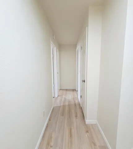 Hallway featuring wood-finish flooring, white painted walls, and white trim