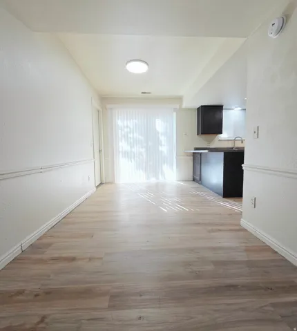 Wood-finish flooring throughout, white walls with wainscoting, and a sliding glass door with vertical blinds