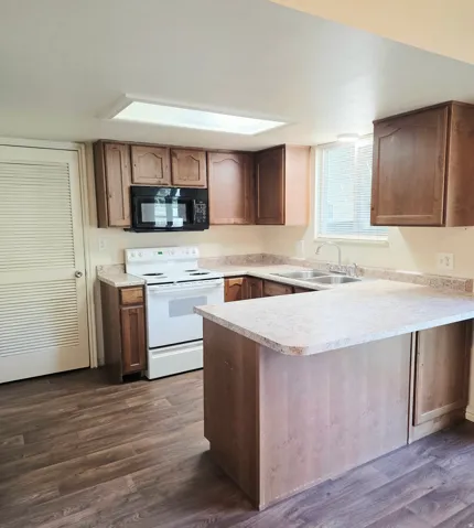 Kitchen featuring wood-finish flooring, wood cabinetry, white appliances, dual basin sink, and an integrated kitchen island