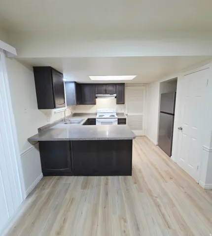 Kitchen featuring dark wood-finish cabinetry, light-toned countertops, stainless steel sink, white range, and light wood-finish flooring