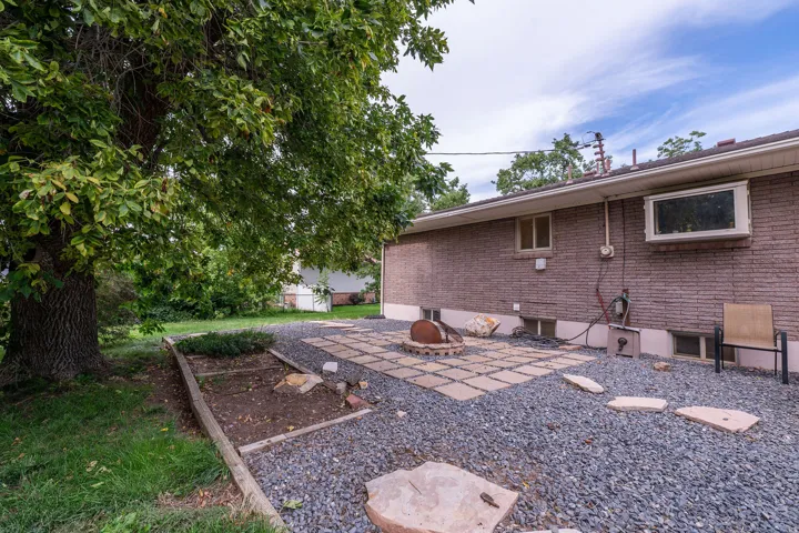 Expansive rear yard featuring a gravel surface, stone stepping pavers, a paver patio area, and a mature tree