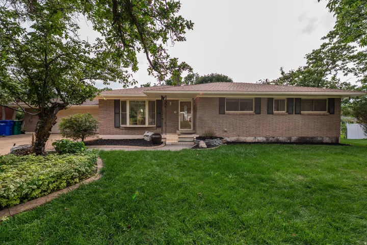 Brick exterior with dark shutters, front entry with transom window, established front yard landscaping, and mature trees
