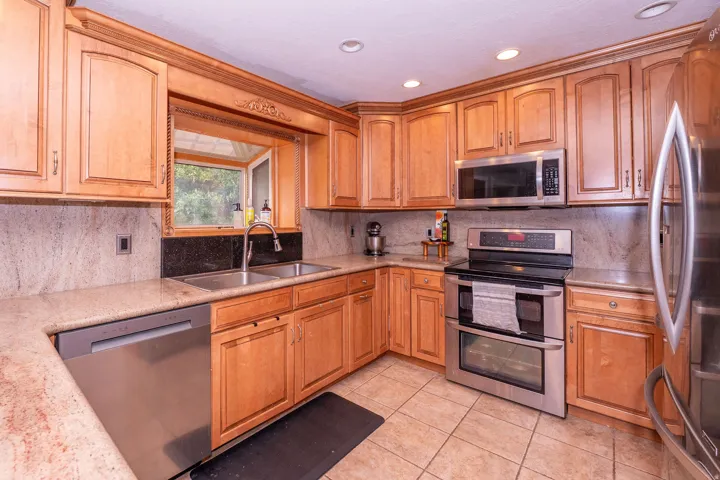 Kitchen featuring wood cabinetry, stainless steel appliances, a double basin sink, and a tile backsplash