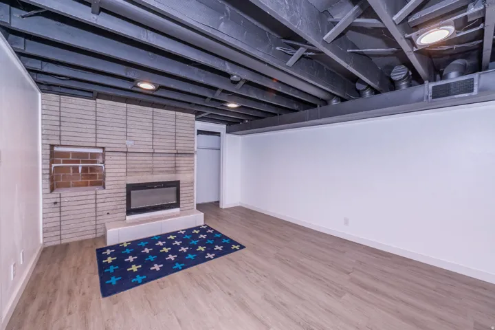 Spacious interior featuring a brick-clad fireplace, wood-finish flooring, and exposed painted ceiling beams