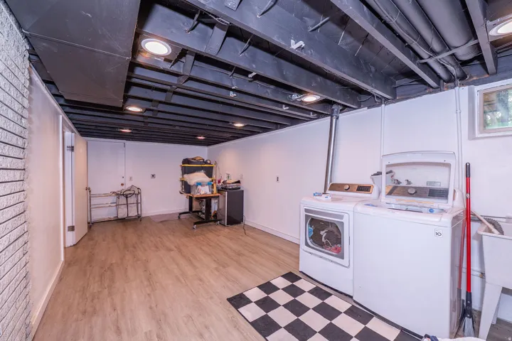 Finished lower level featuring recessed lighting, exposed ceiling beams, wood-finish flooring, and white painted brick