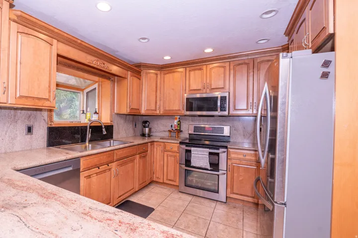 Kitchen featuring warm wood cabinetry, neutral stone countertops, stainless steel appliances, and a double basin sink