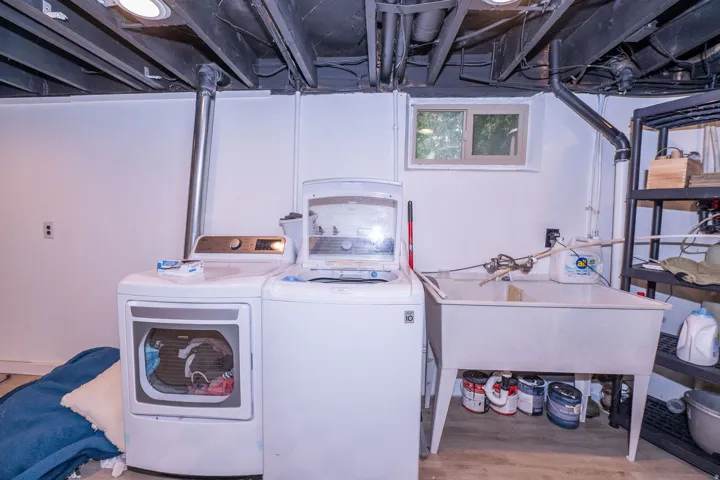 Utility space featuring an exposed painted ceiling, a single window, a utility sink, and wood-finish flooring