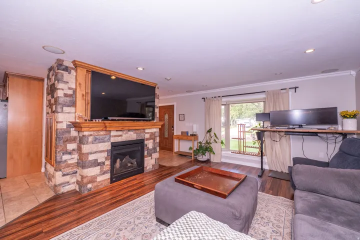 Stone-clad fireplace with wood mantel, wood-finish flooring, recessed lighting, and crown molding