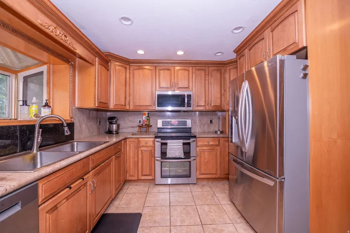 Wood-finish cabinetry, stainless steel appliances, tiled backsplash, dual basin sink, and recessed lighting