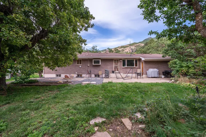Brick exterior with a concrete patio, framed by mature trees, and a mountain backdrop