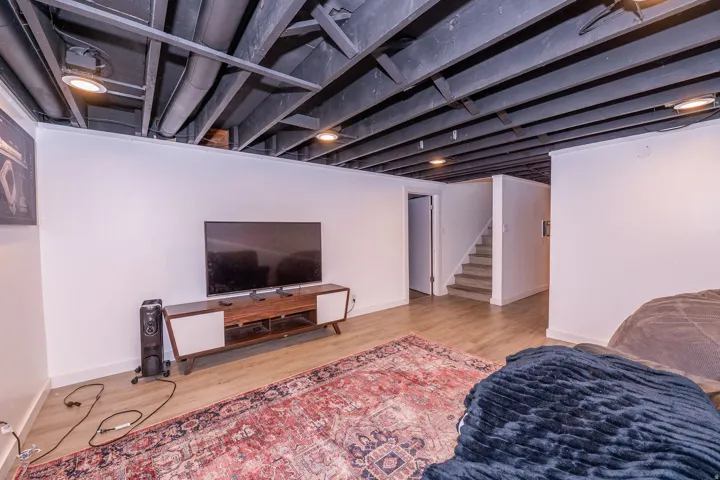 Wood-finish flooring, white walls, exposed ceiling with dark beams, and recessed lighting