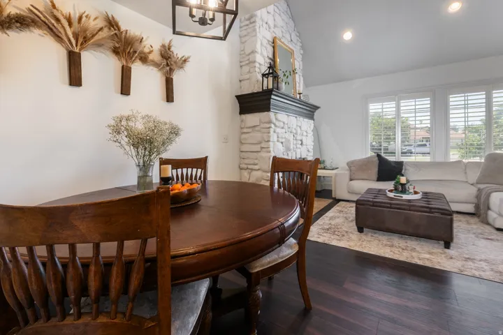 Hardwood-style flooring, white stone fireplace with dark wood mantel, high vaulted ceiling, recessed lighting, and plantation shutters