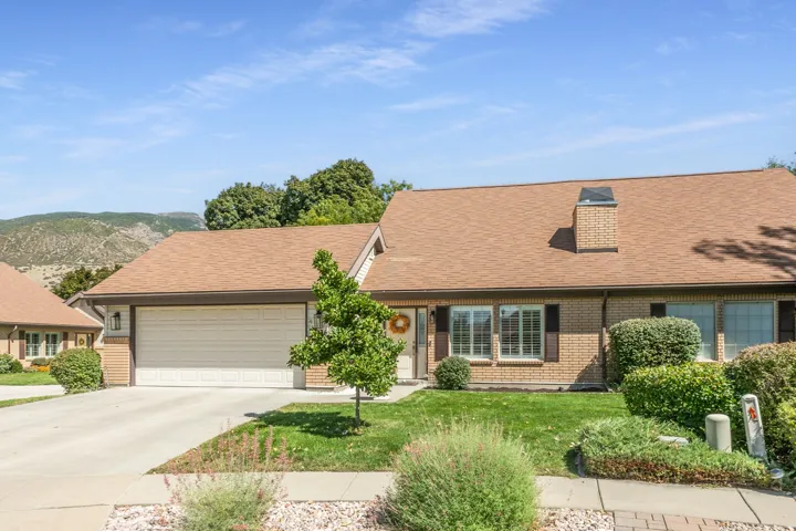 Brick-clad exterior with a brown shingle roof, attached garage, and a concrete driveway