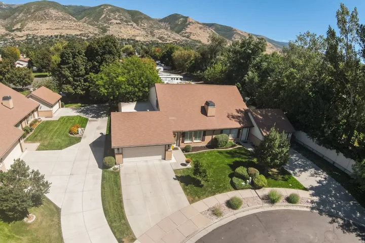 Expansive concrete driveway, attached two-car garage, manicured front lawn, mature landscaping, and mountain backdrop