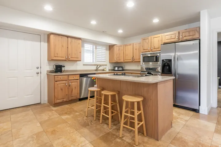 Kitchen with wood cabinetry, stainless steel appliances, a center island, recessed lighting, and tile flooring