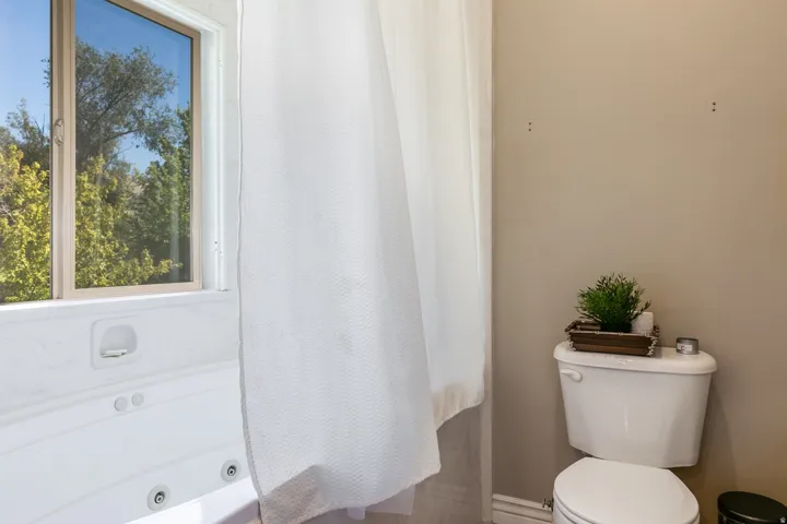 White jetted tub with a window, showcasing a neutral-toned wall and a white toilet