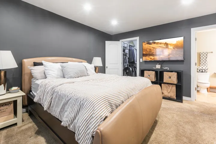 Wall-mounted television with built-in shelving, soft carpet flooring, recessed lighting, and a walk-in closet with built-in organization