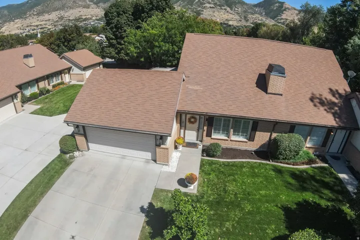 Front elevation featuring a brick facade, attached garage, concrete driveway, and mature landscaping