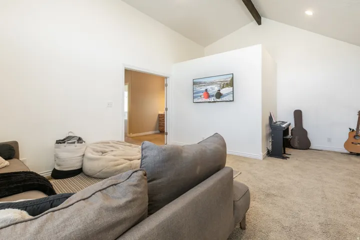 Vaulted ceiling with exposed beam, recessed lighting, and carpeted flooring