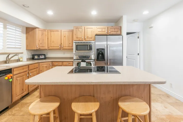 Kitchen featuring wood-finish cabinetry, stainless steel appliances, an island with an integrated cooktop, and light-colored countertops