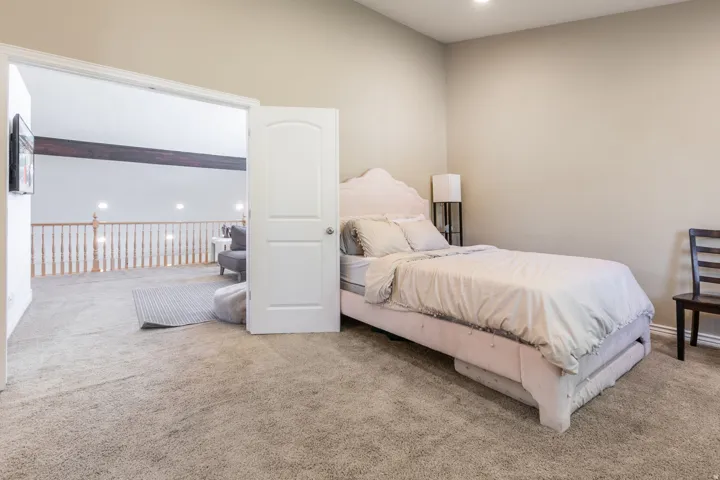 Carpeted flooring extending through a wide doorway to an open loft area with a wood beam ceiling accent