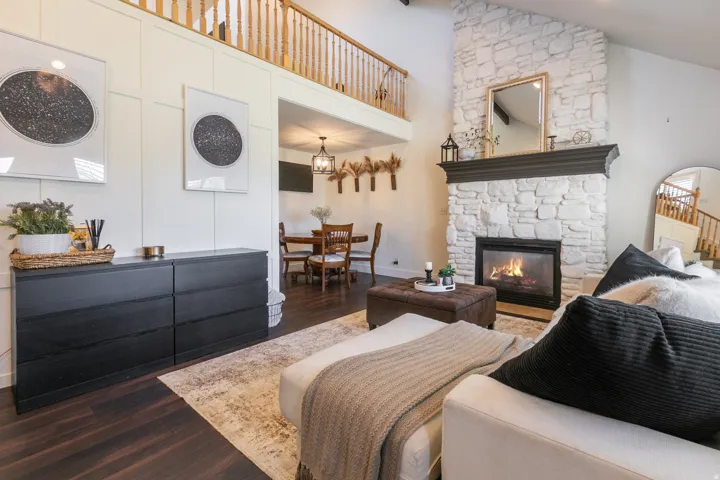 Vaulted ceiling, stone-clad fireplace with mantel, dark wood-finish flooring, and a second-story balcony with wood railing