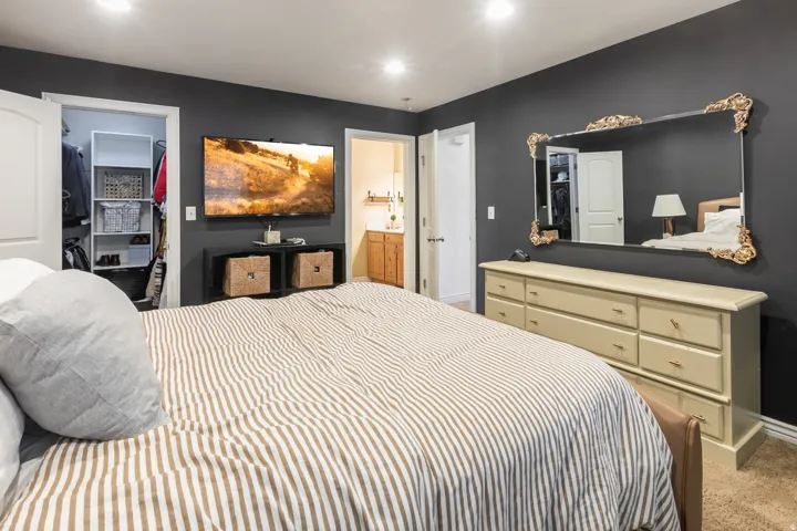 Recessed lighting illuminates a space featuring a walk-in closet with built-in shelving, a dresser with multiple drawers, and a large wall-mounted mirror