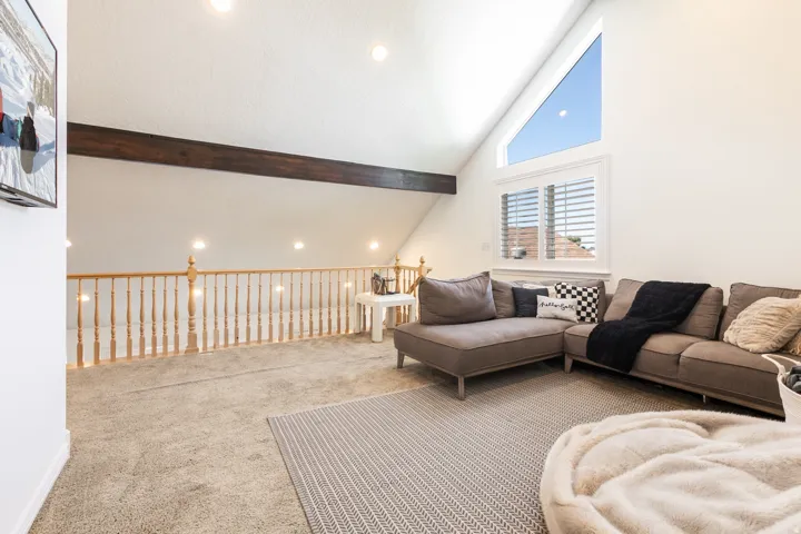 Vaulted ceiling with exposed wood beam, large triangular window, white window shutters, light wood baluster railing, and recessed lighting