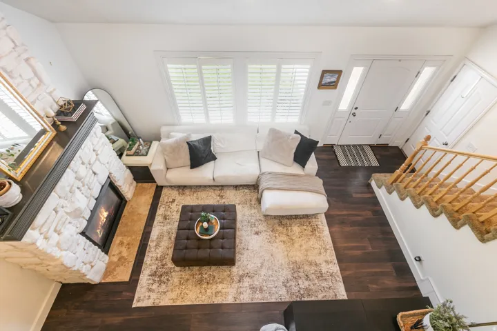 Stone-clad fireplace with dark wood mantel, rich wood-finish flooring, white window shutters, and a front entry door with transom and sidelight windows