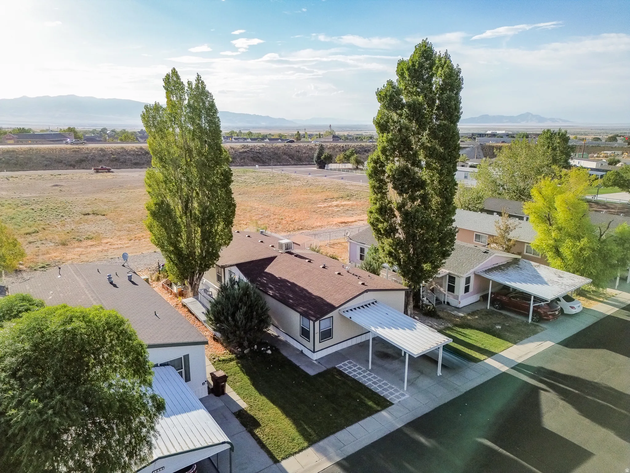 Single-story residence featuring a covered carport, manicured lawn, and mature trees