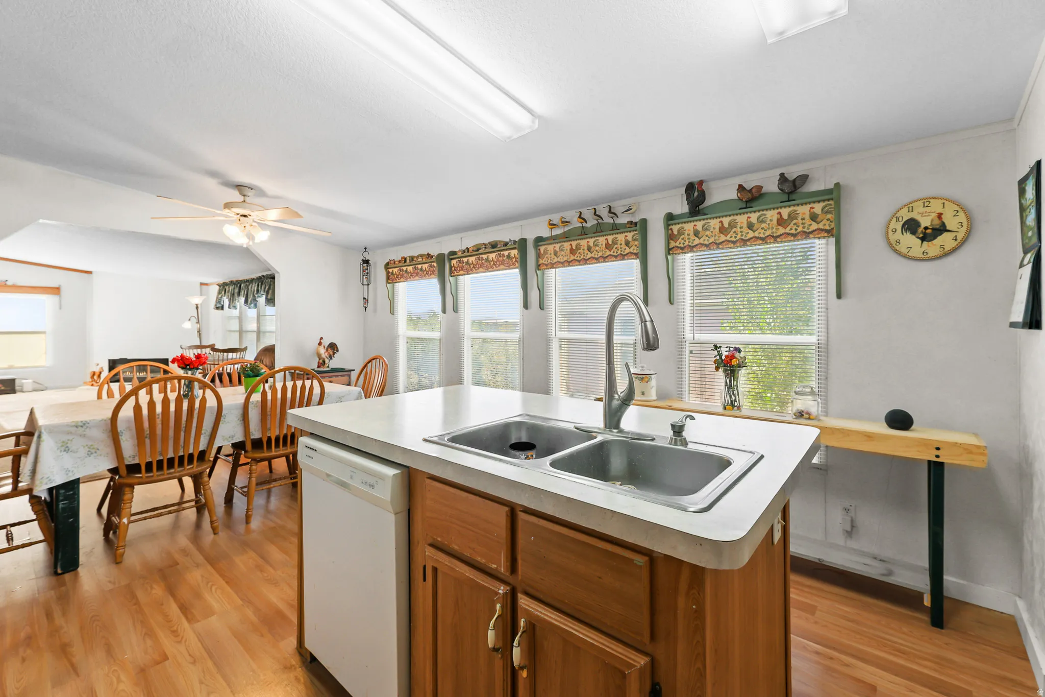 Kitchen island with integrated double basin sink and a single-handle faucet, wood-finish flooring, and multiple windows with blinds