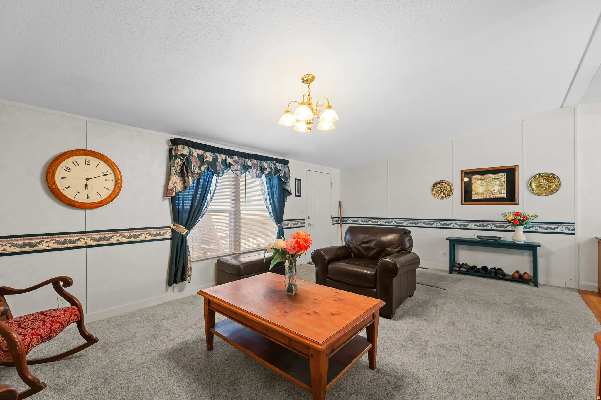 Recessed window, gold-toned chandelier, light-colored panel walls, and gray carpeting