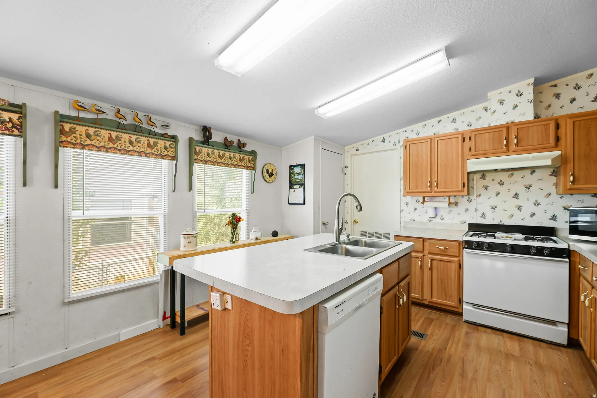 Kitchen featuring a central island with an integrated double basin sink, light wood-finish cabinetry, a gas range, and wood-finish flooring