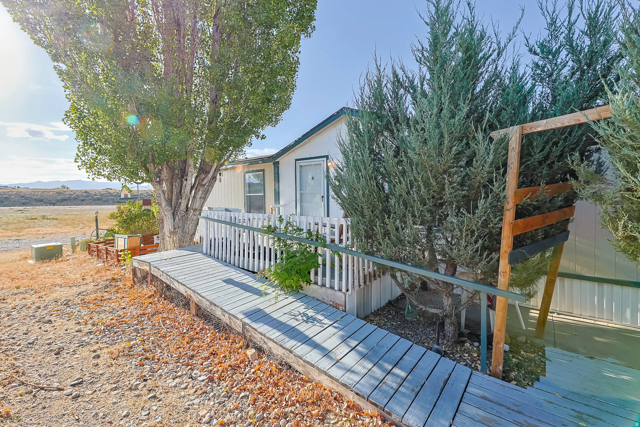 Exterior featuring a white picket fence, wooden ramp, mature trees, and a gravel driveway