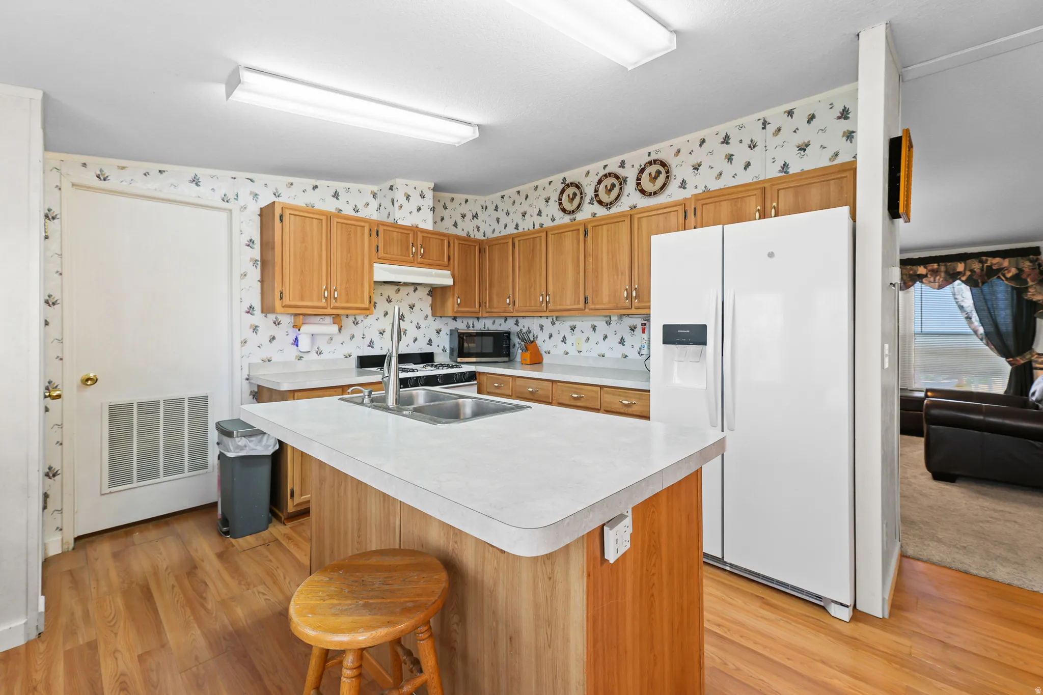 Kitchen featuring wood-finish flooring, an island with integrated sink, wood cabinetry, and a full suite of appliances
