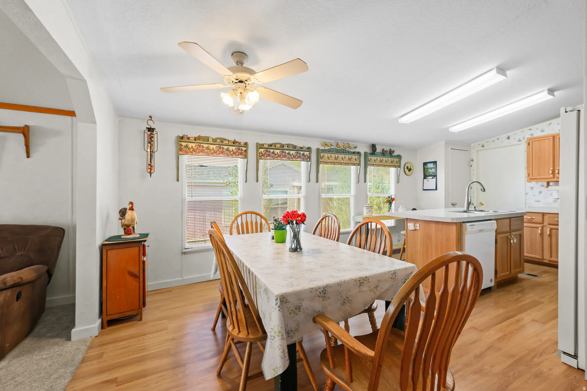 Open-concept living space with wood-finish flooring, a ceiling fan, and multiple windows