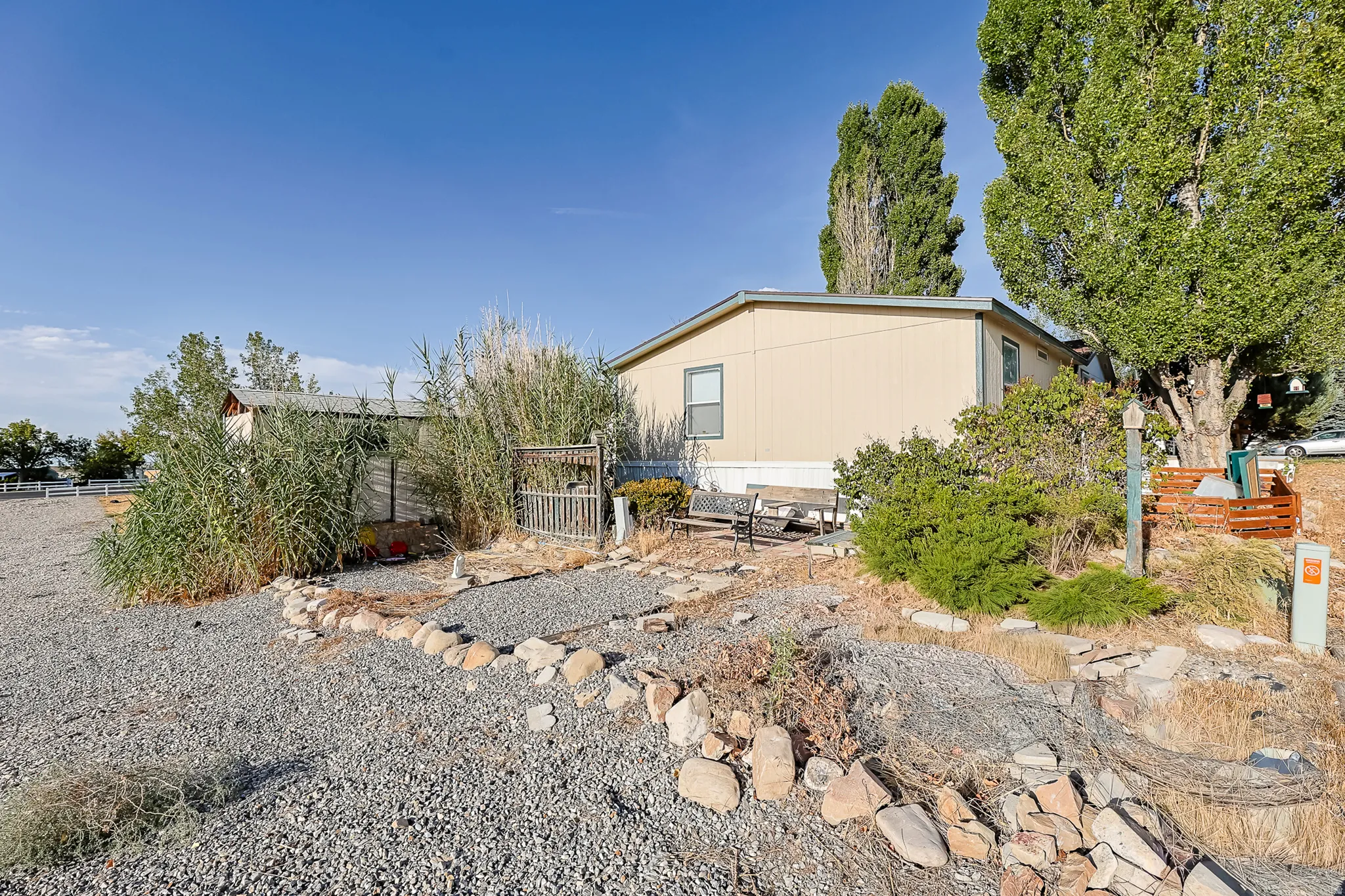 Gravel landscaping with a rock border, mature trees, and an exterior shed