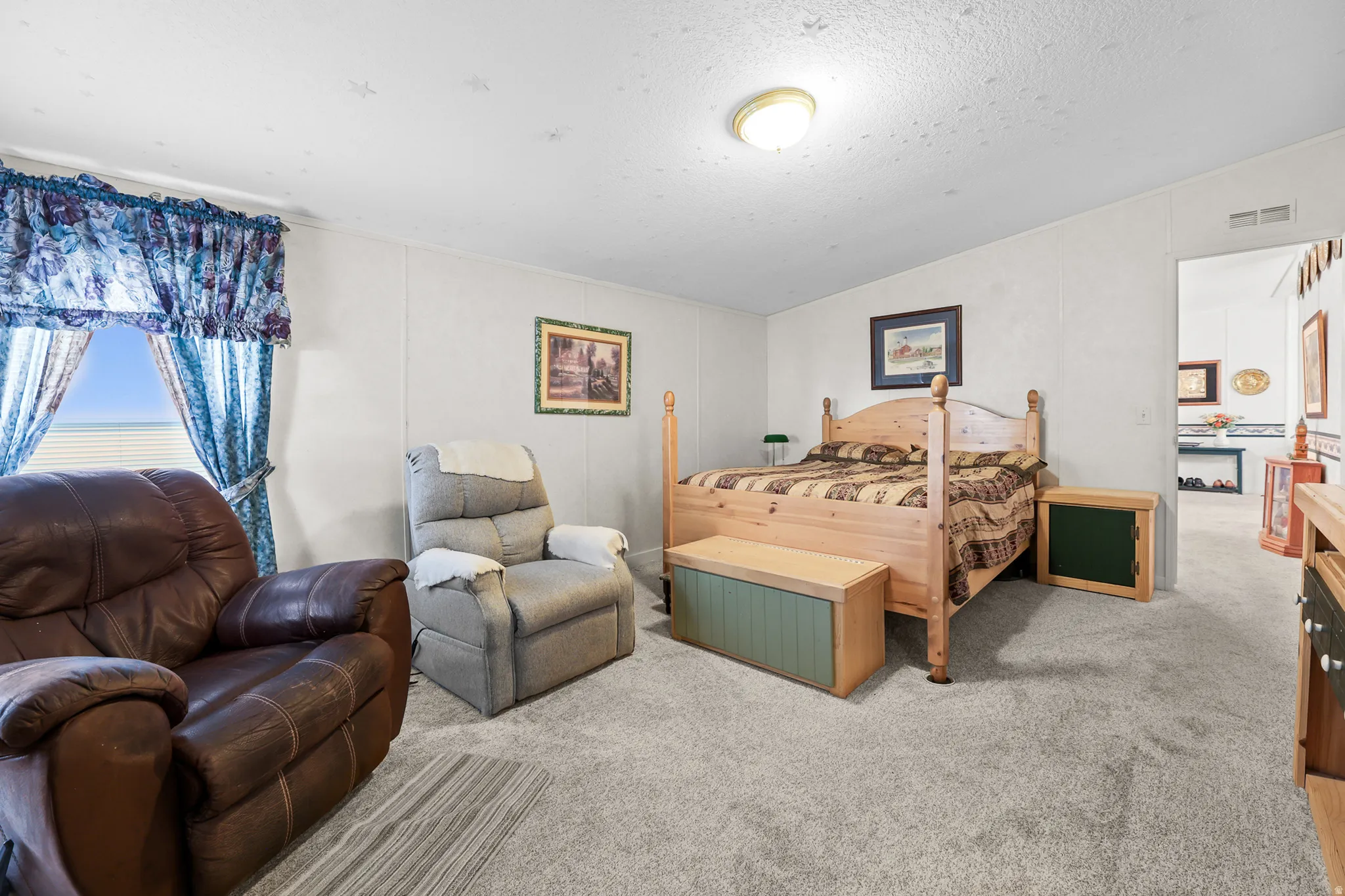 Carpeted flooring, window with blinds, wall-mounted light fixture, and an entry to an additional space