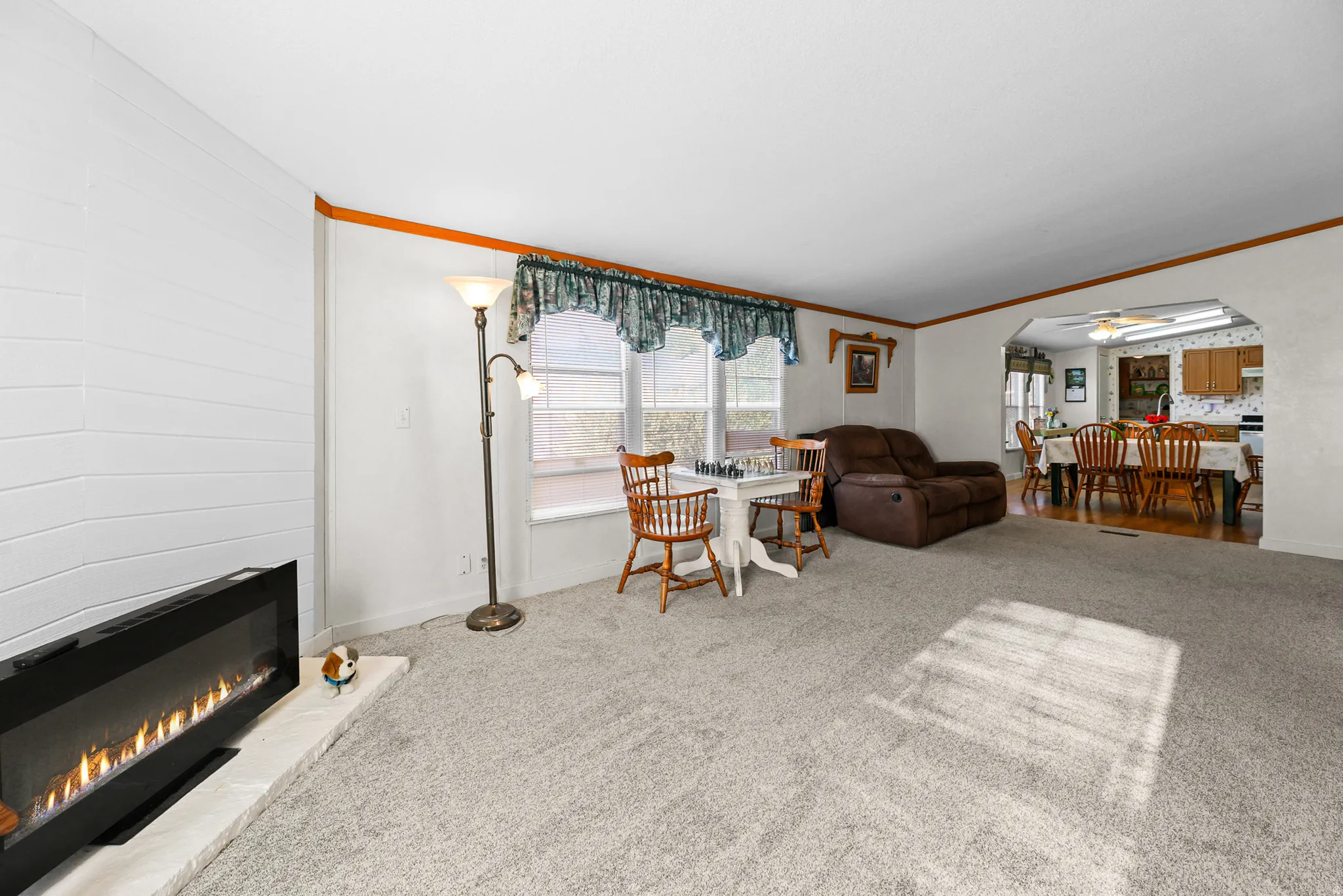 Living area with carpet flooring, a built-in electric fireplace, and window with valance