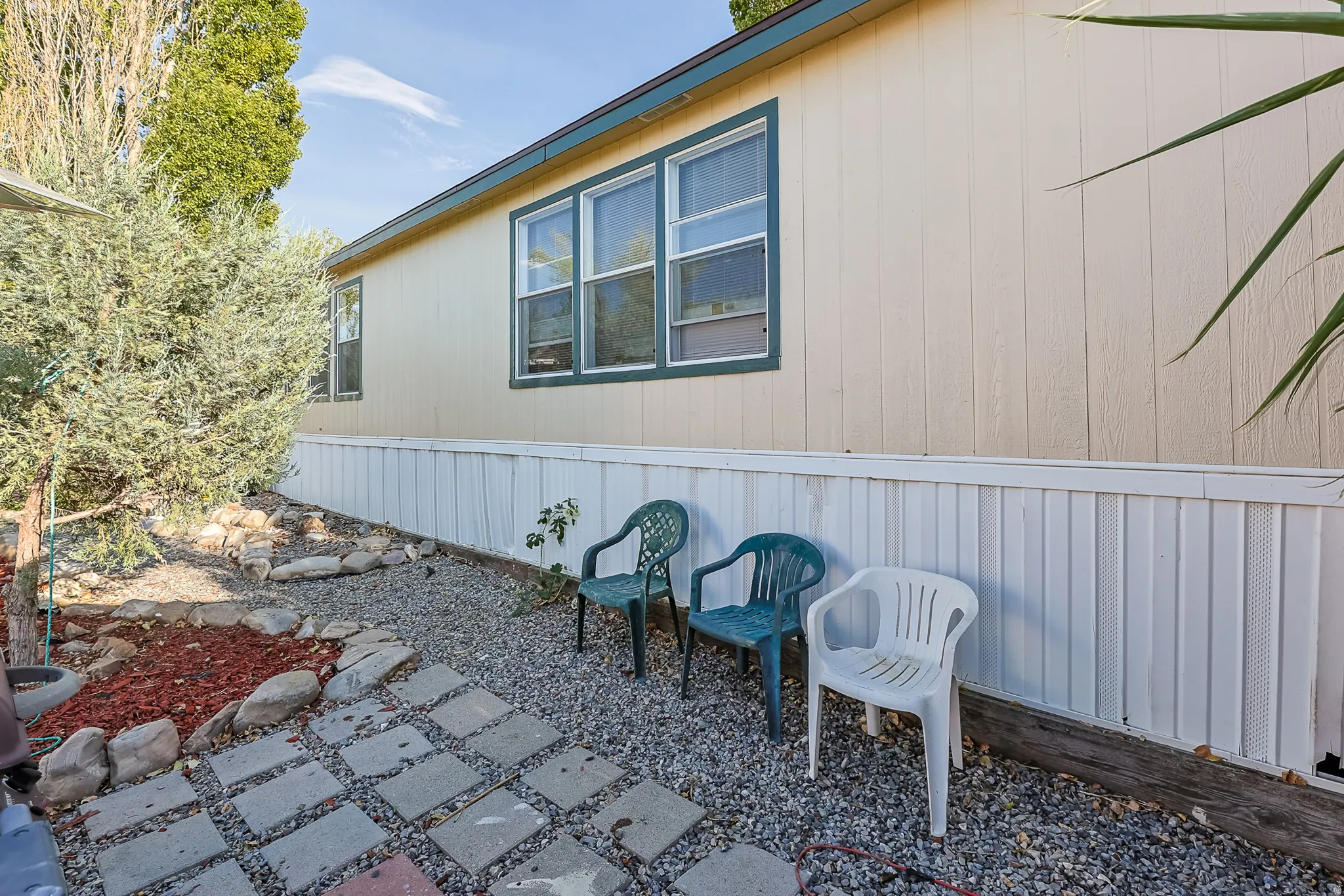 Exterior siding with multiple windows, surrounded by landscaping featuring gravel and stepping stones
