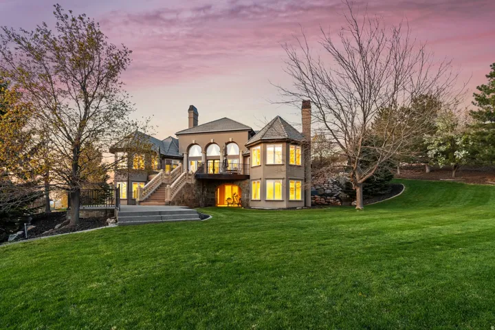 Expansive green lawn surrounds a multi-level stucco exterior with arched windows, a private balcony, and stone staircase