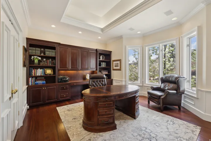 Built-in custom cabinetry with integrated desk space, bay window with multiple panes, tray ceiling, recessed lighting, and wood-finish flooring