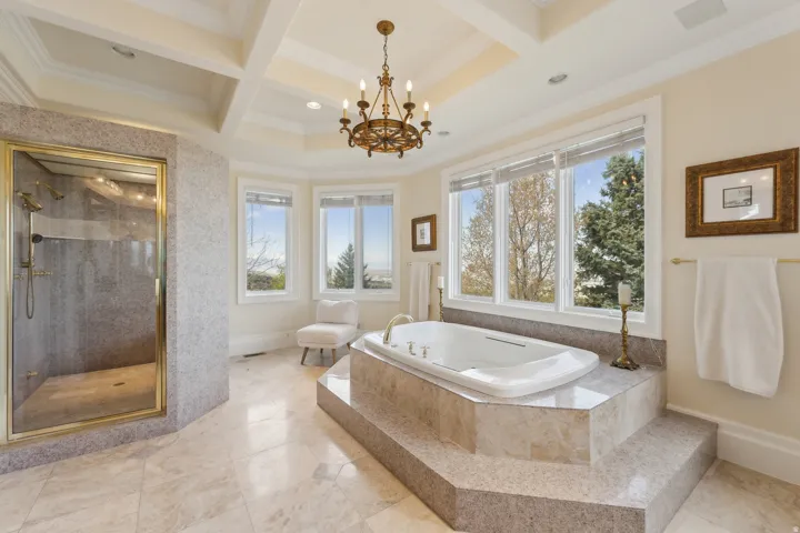Soaking tub with stepped surround, multiple windows, coffered ceiling, chandelier, and a glass-enclosed shower
