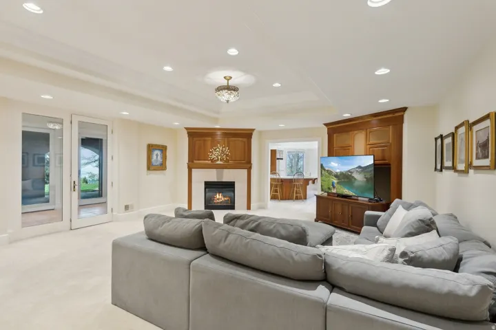 Recessed lighting, wood-finish fireplace surround with a stone hearth, glass-paneled French doors, coffered ceiling, and built-in cabinetry