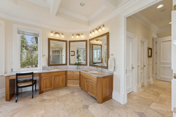 Corner vanity with light wood cabinetry, multiple mirrors, and dual sinks